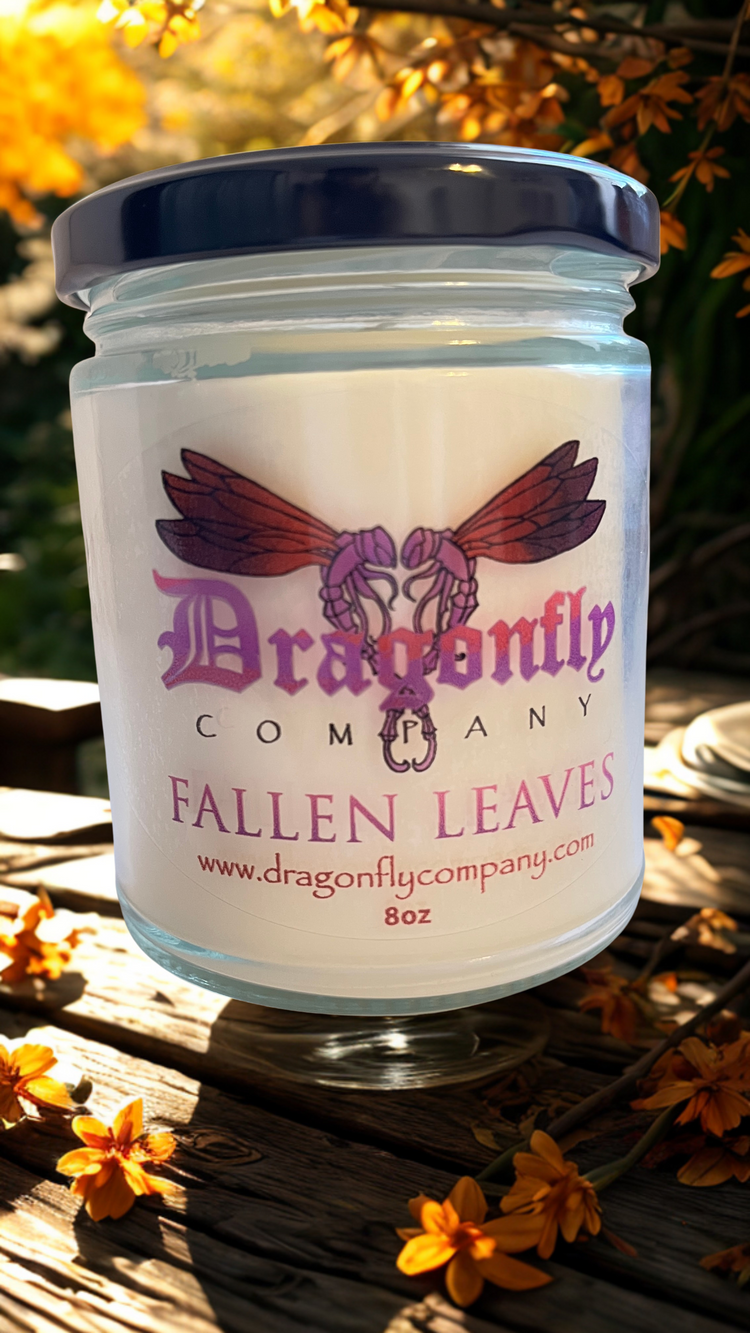 Jar of 'Fallen Leaves' candle from Dragonfly Company on a wooden surface with flowers.
