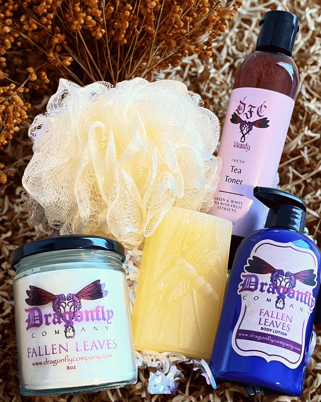 Set of Dragonfly Company products including a candle, soap, lotion and tea toner on a textured surface.