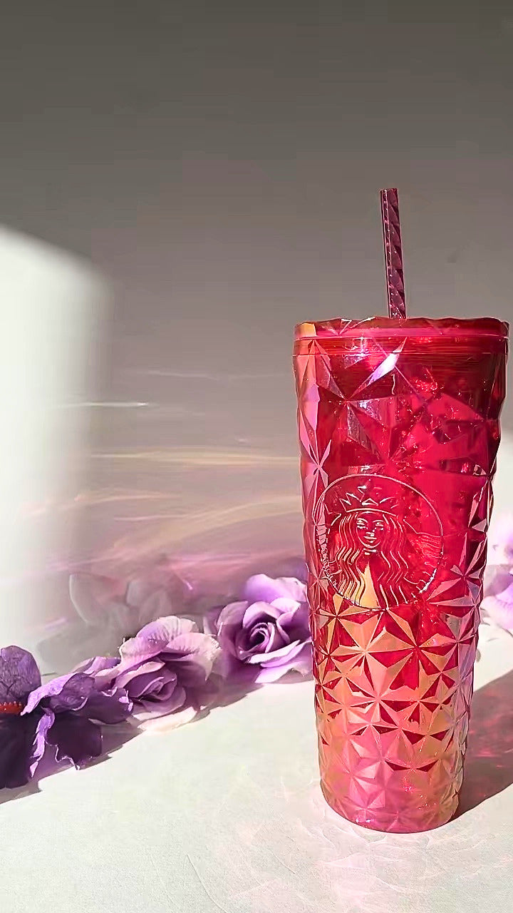 A red faceted textured tumbler cup with a matching red striped straw, featuring an embossed Starbucks siren logo, set against a light gray background with decorative purple flowers on the left.