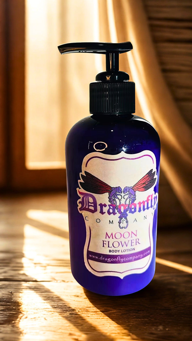 A bottle of Dragonfly Company Moon Flower Body Lotion on a wooden surface with warm sunlight and shadows.