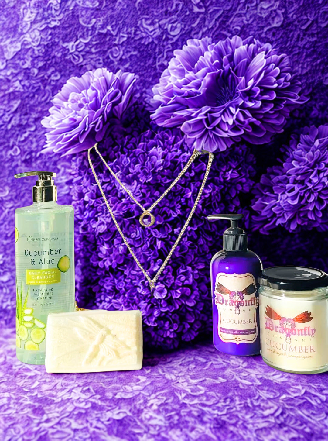 Cosmetic products including a lotion, soap, candle cucumber facial cleanser and necklace on a purple floral background