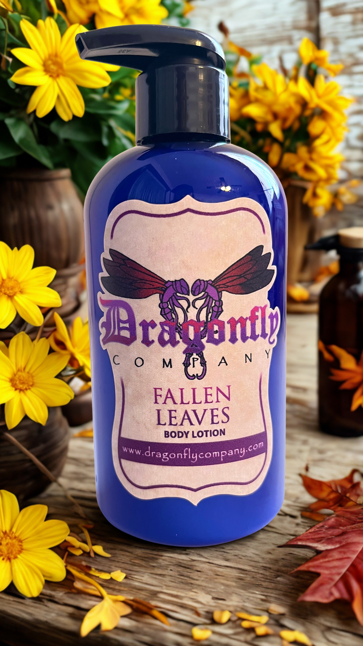 Blue bottle of 'Fallen Leaves' body lotion from Dragonfly Company with autumn leaves and flowers in the background.