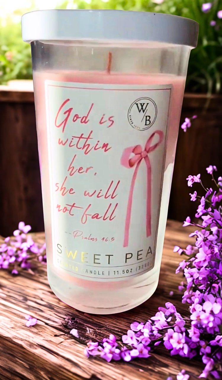 God is within her Candle with text and branding on a wooden surface with flowers