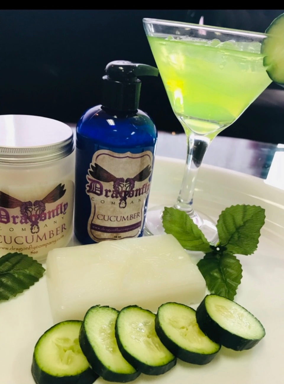 Cucumber-themed products including a bottle, jar, sliced cucumbers and cucumber soap on a white surface.