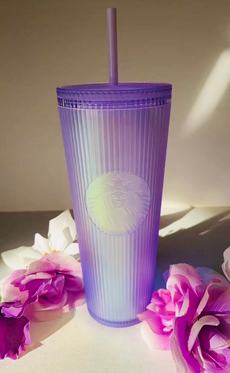 Purple Starbucks tumbler with a straw on a light surface with flowers.