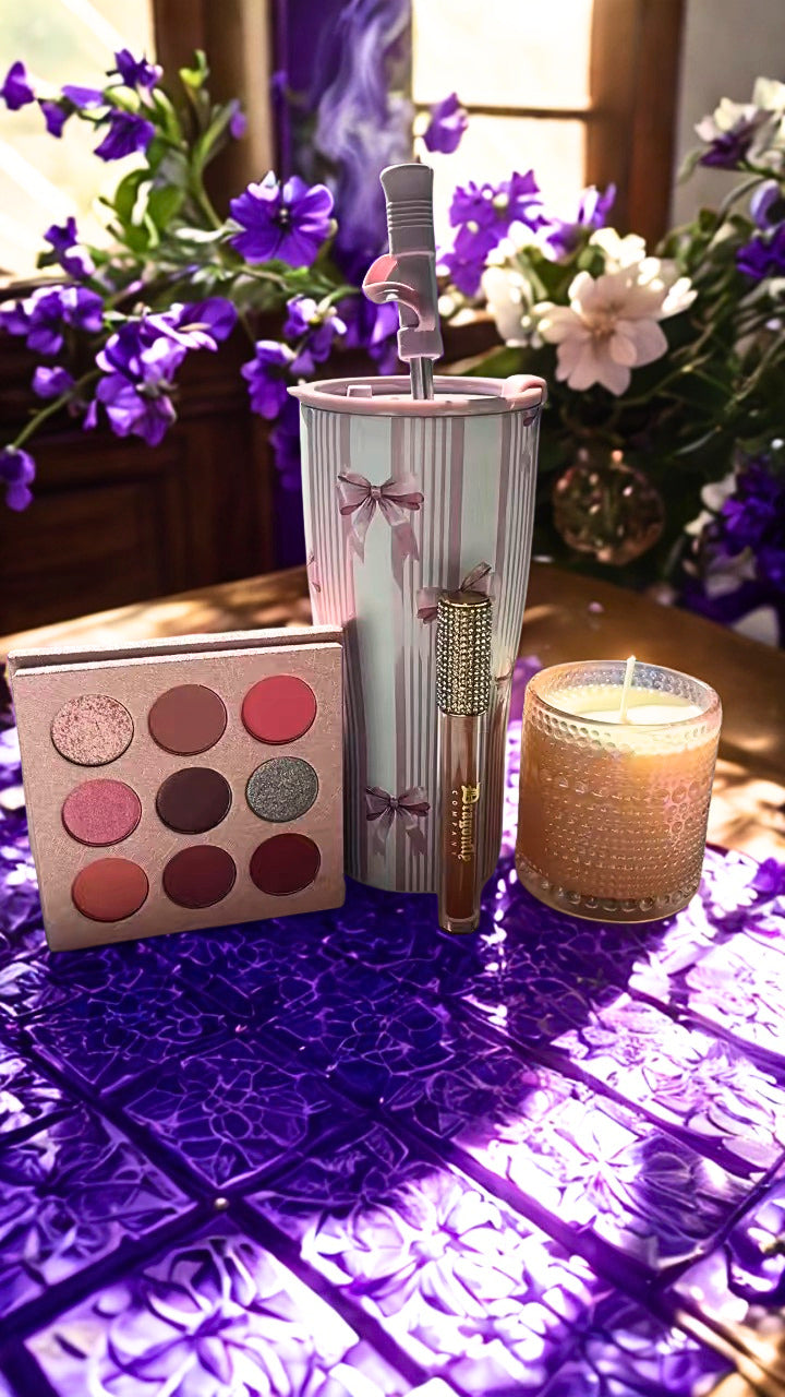 My princess collection is including a eye shadow palette, lip gloss, tumbler and candle on a textured purple surface with flowers in the background.