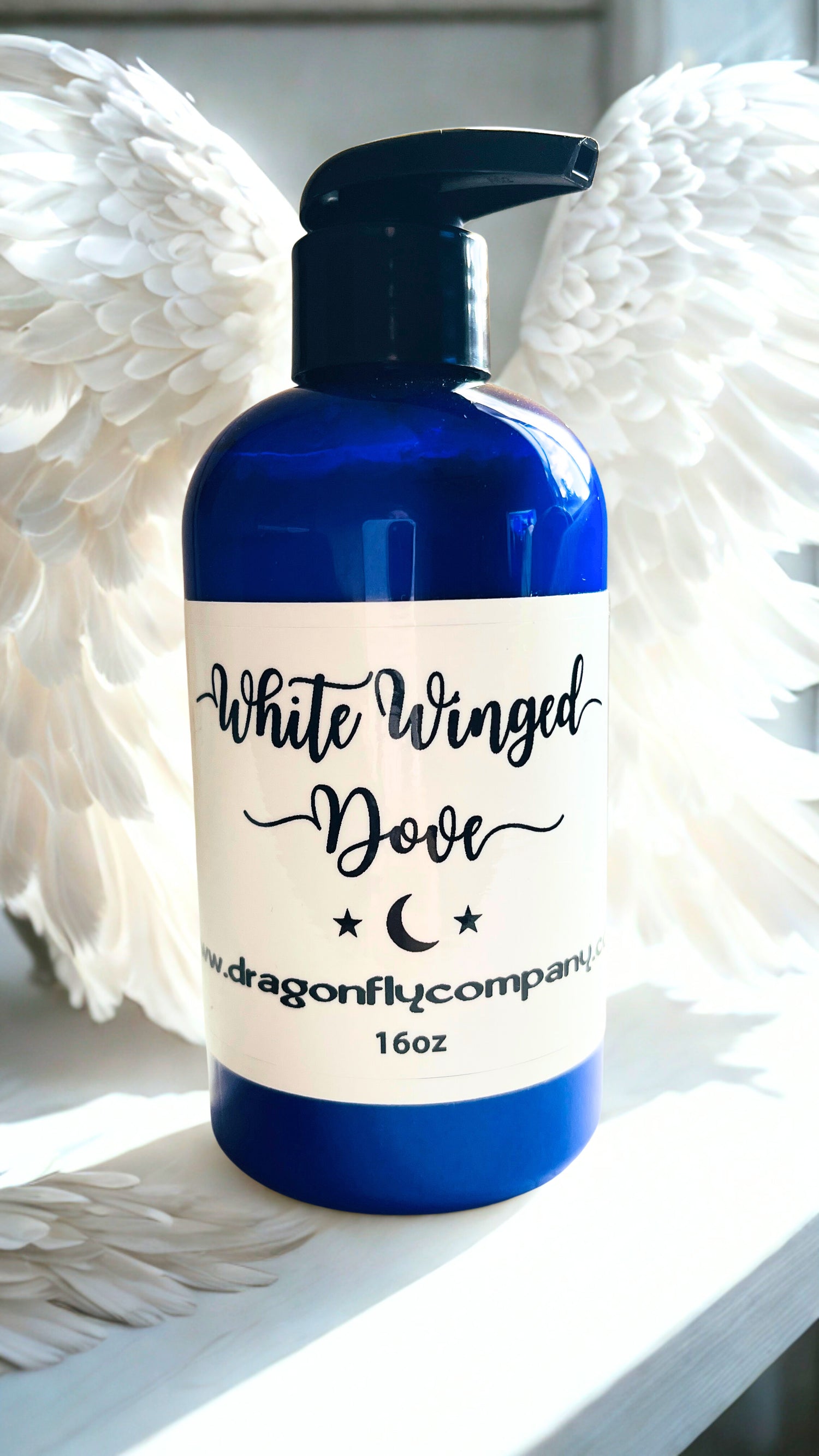 Blue bottle of lotion with a label reading 'White Winged Dove' on a white surface. 