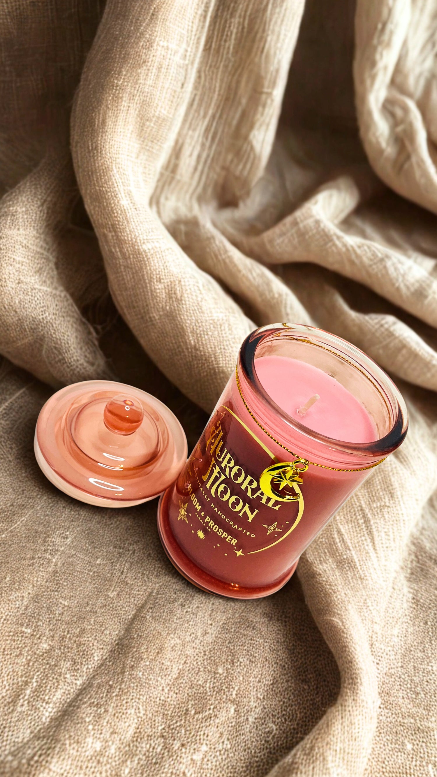 Pink scented  candle with a decorative label on beige fabric