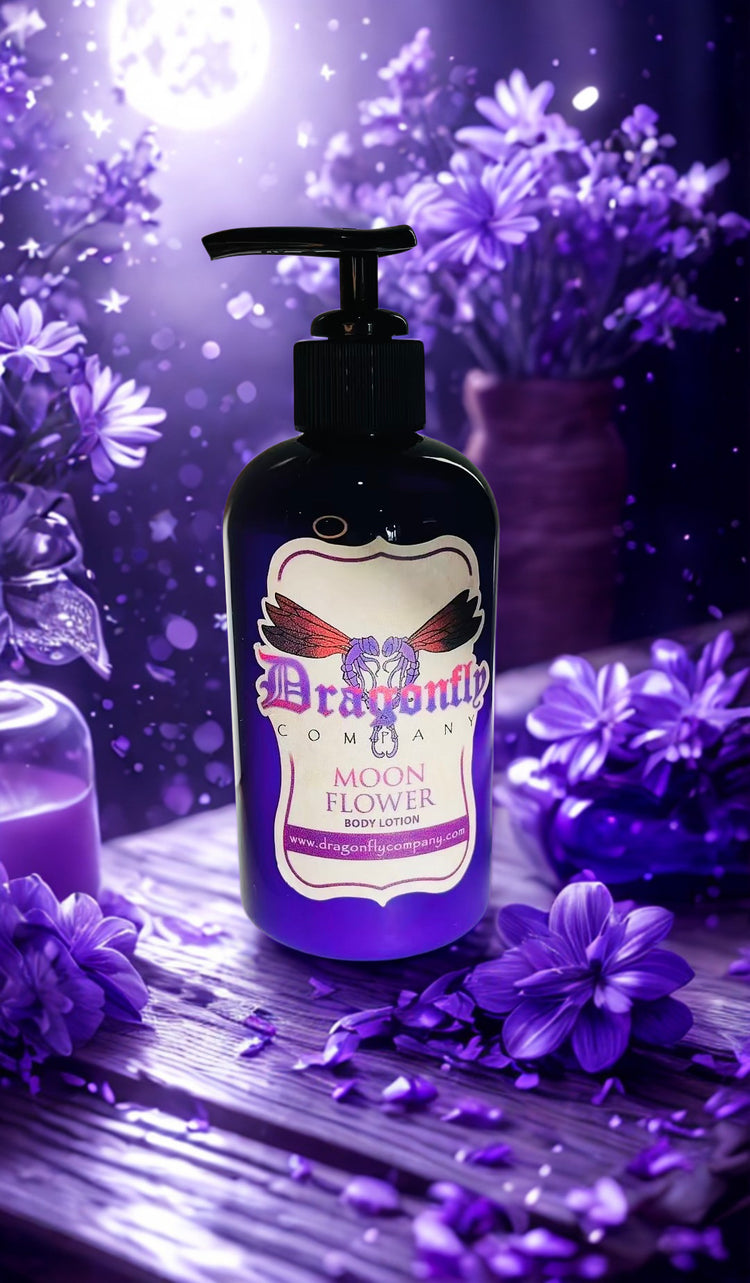 A bottle of Dragonfly Company Moon Flower body lotion sits on a wooden surface surrounded by purple flowers and glowing purple lighting.